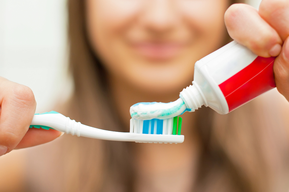 close up of woman putting toothpaste on toothbrush