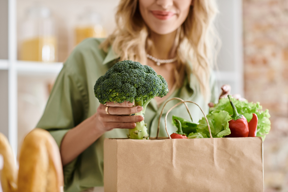 woman taking a bunch of broccoli out of a brown grocery bag