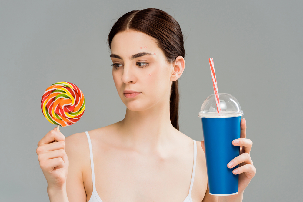 woman holding a lollipop and milkshake, deciding between the two