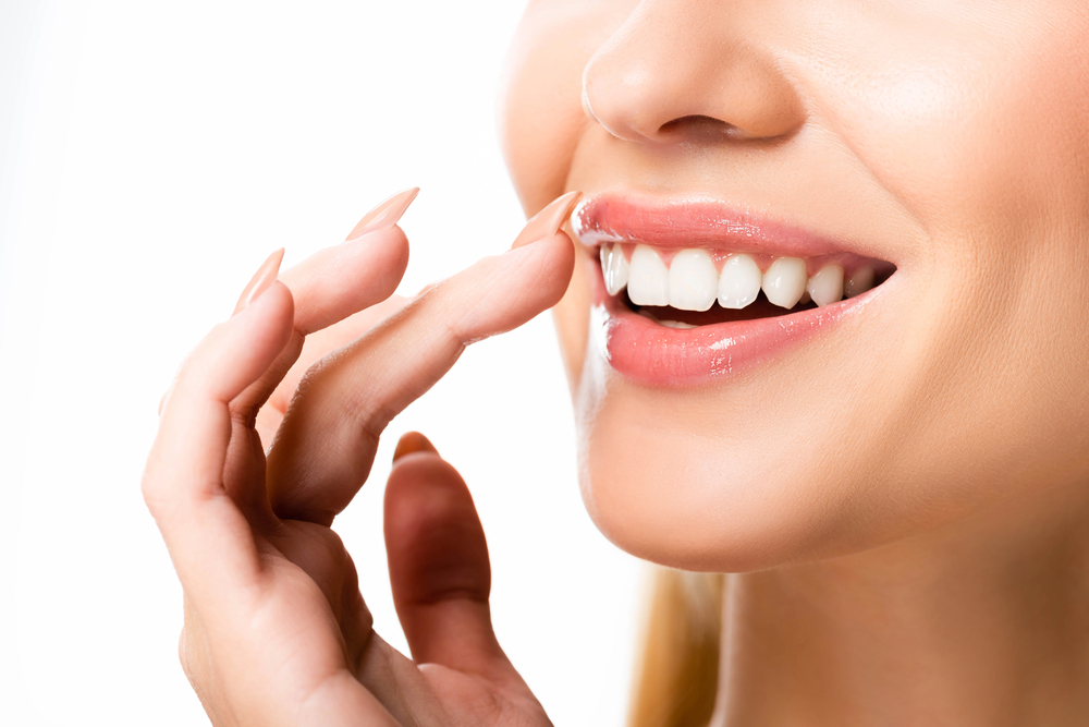 close up of woman smiling after teeth whitening, touching her top lip